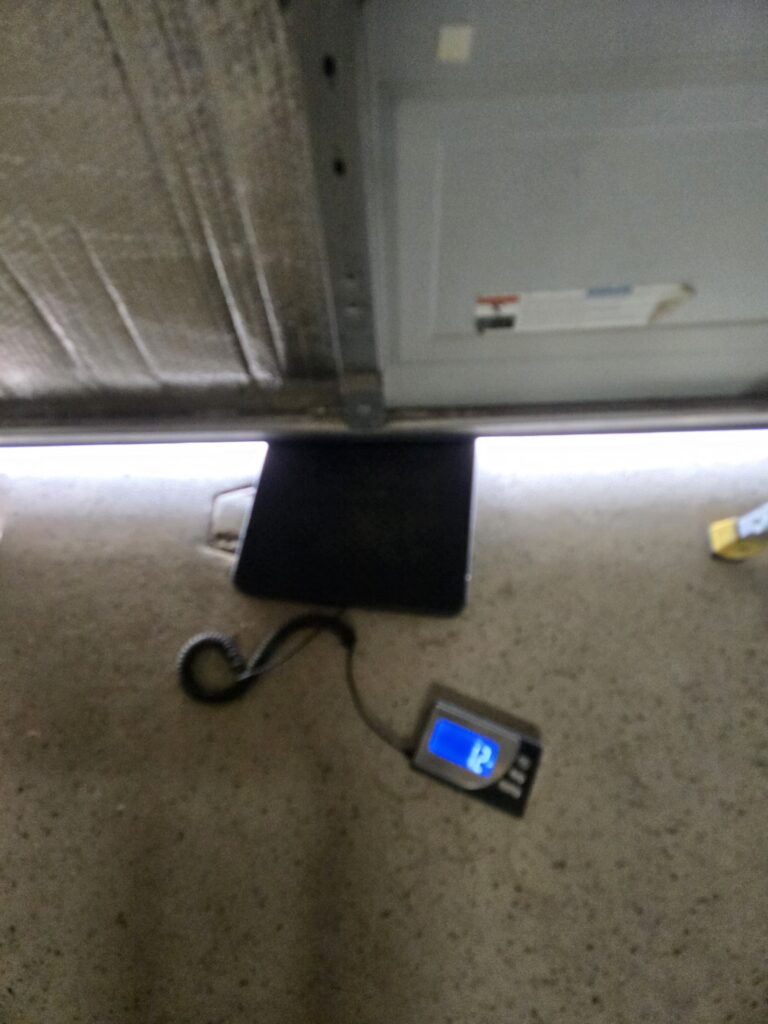 Technician at Garage Door Grunts weighing a garage door to ensure torsion springs and door are properly balanced - Door exceeds 5lbs of weight - meaning the garage doors springs are fatigued and need tightening or replaced